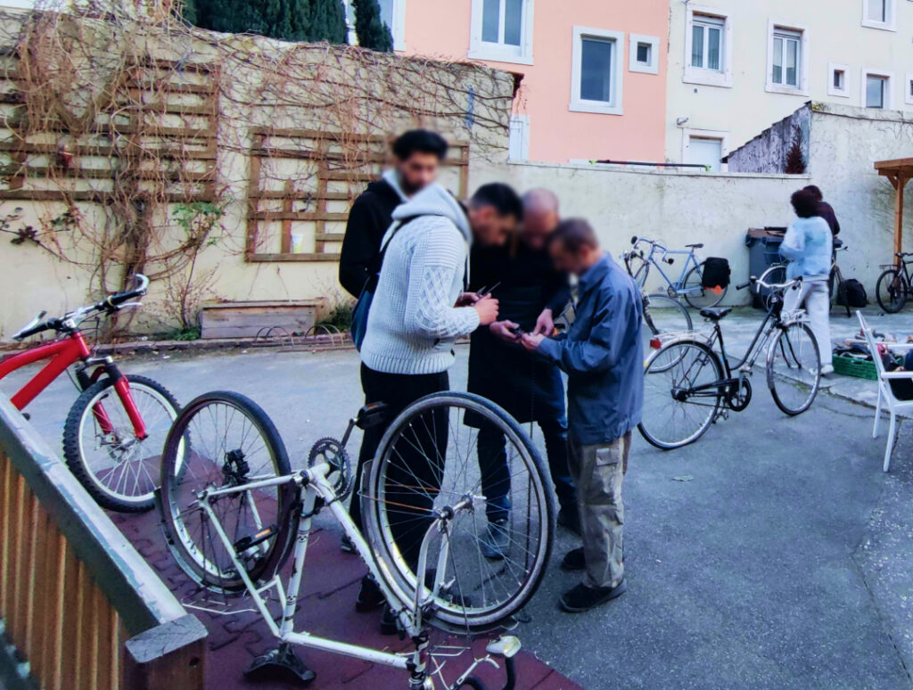 Un groupe de personne en train de travailler ensemble sur une chaîne de vélo. Au milieu de la cour, avec plusieurs vélos en train d'être réparés autour.