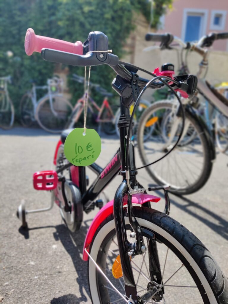 Une photo d'un vélo pour enfant rose, avec une étiquette verte indiquant "10€, réparé"